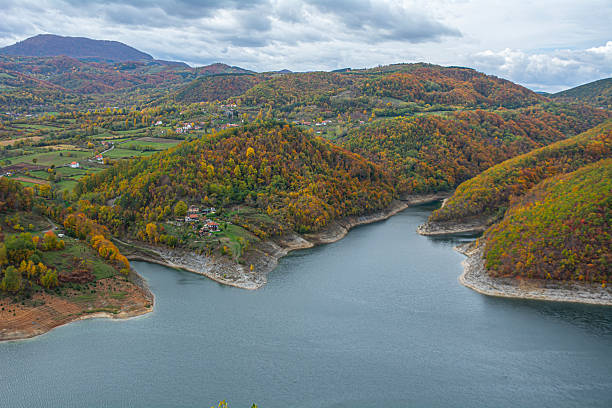 istock Tranquil Lake Winding Through Autumn Hills with Scattered Houses and Fields Under a Cloudy Mountain Sky 2247438460