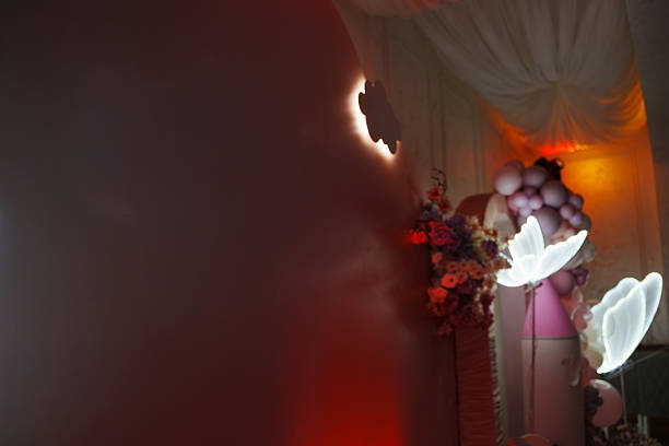 Colorful butterflies float in the air, surrounded by floral arrangements and balloons at a festive event in a warmly lit indoor space.