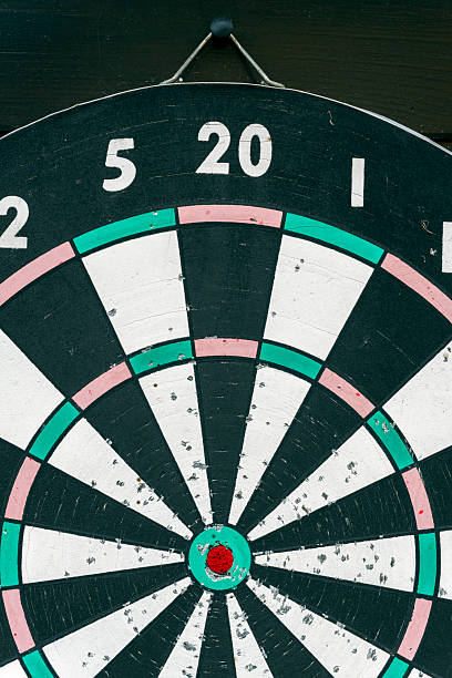 Dart board with darts showing one in the bullseye. Shows a realistic result. Moderate precision and moderate accuracy.