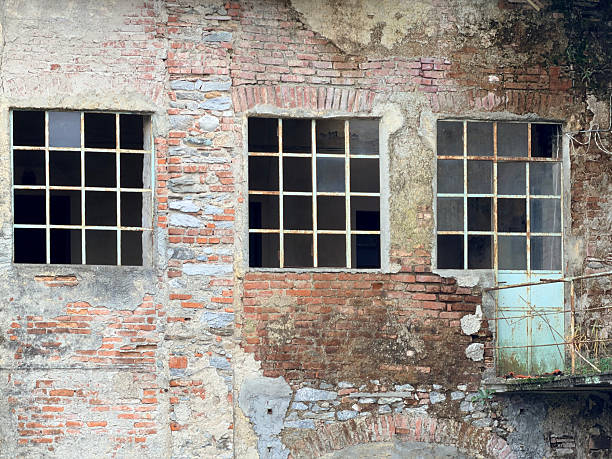 An abandoned industrial structure with exposed brickwork, deteriorated plaster, and rusted window frames. The scene highlights textures of decay and the fading architectural heritage of rural Italy.