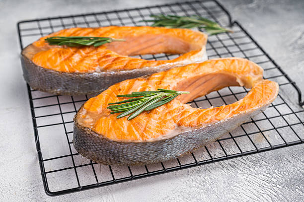 istock Two cooked salmon slices with herbs resting on a metal grid against a soft gray surface for fresh clean modern food styling. 2247452364