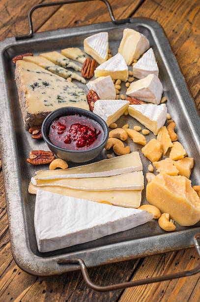 Gourmet cheese platter with assorted textures and nuts arranged on vintage metalware over a wooden background.