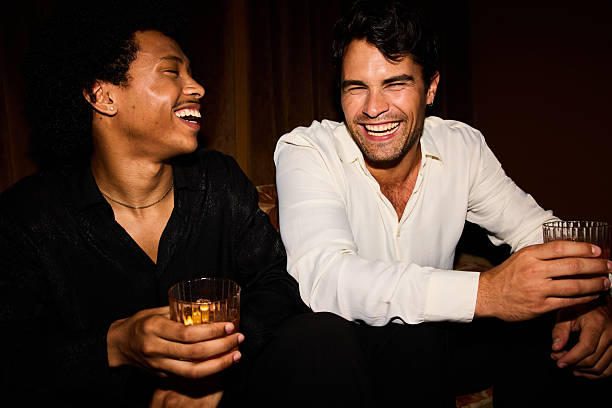 istock Two happy young men enjoying conversation and laughing while holding drinks at a party 2247453795