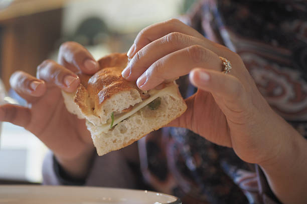 Close-up of people enjoying Italian ham and cheese sandwiches wrapped in paper with Caprese salad on the table.