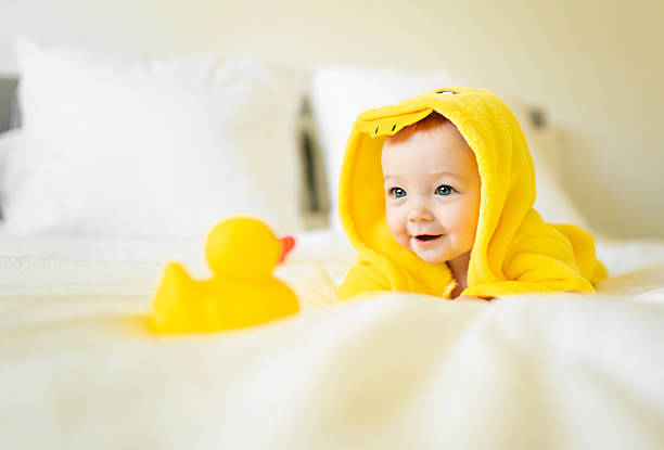 A baby wearing yellow hooded duck towel on parents bed after bath