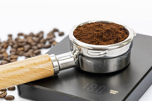 istock Portafilter with finely ground coffee on digital kitchen scale showing 18 grams weight beside scattered coffee beans on white 2247461524