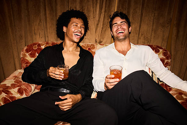 Two joyful young men laughing and relaxing on a sofa with drinks during a cheerful New Year’s Eve celebration