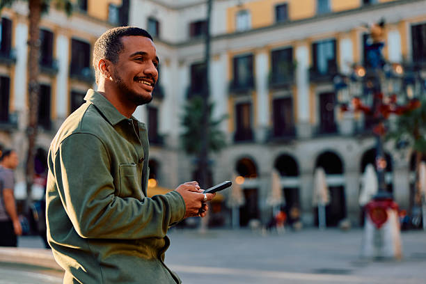 istock Young man smiling using smartphone in city square 2247470686