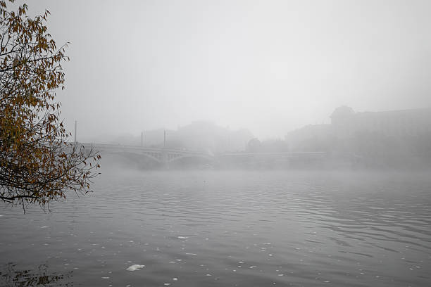 Vltava river flowing through thick fog covering Manes bridge and Rudolfinum, creating a mysterious atmosphere in prague