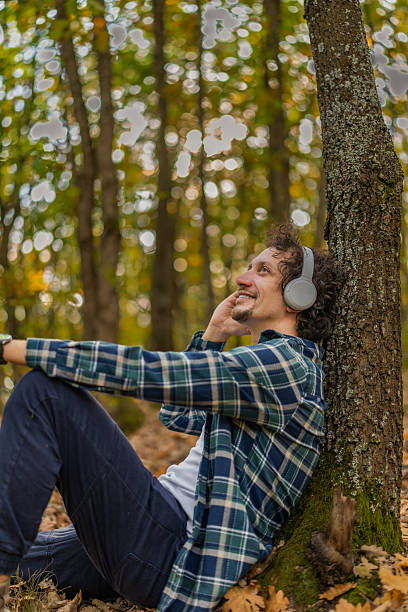istock Man with wavy hair resting in nature, leaning on a tree trunk and talking on his smart phone while enjoying in the autumn day. 2247472995