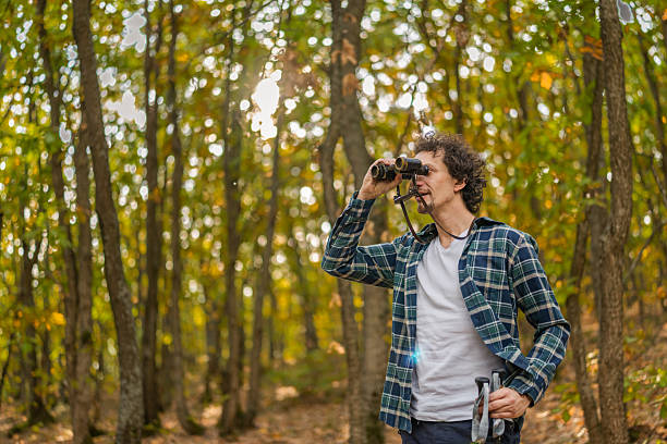 istock Man with wavy hair using binoculars in the forest in the autumn day. 2247474091