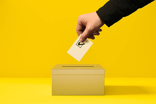 A person putting a voting card into a yellow ballot box.