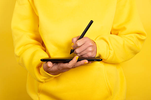 istock Person in yellow sweater using digital drawing tablet and stylus. Modern creative workspace with monochrome color scheme, ideal for tech and design themes. 2247481083