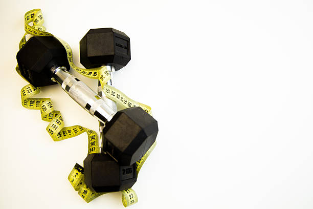 istock Black dumbbells resting on a white surface surrounded by a yellow measuring tape, symbolizing fitness, health, and personal training goals for a healthy lifestyle 2247485310