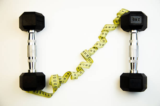 istock Black dumbbells positioned on a white background with a yellow measuring tape creatively arranged between them, symbolizing fitness, health, and personal training goals 2247486044