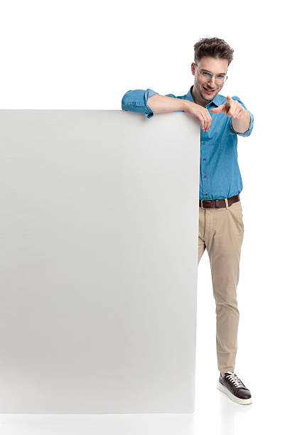 istock Happy casual man pointing finger while leaning on billboard 2247487954