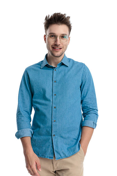 Happy young casual man with glasses in blue shirt smiling with one hand in his pocket, isolated on white background.