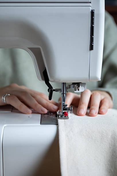 istock woman sewing beige fabric on sewing machine, front view 2247488810