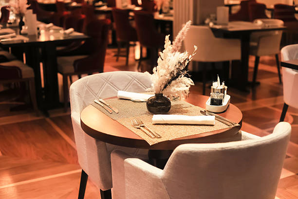 istock A sophisticated restaurant interior with an intimate table setting, plush chairs, warm lighting, and decorative dried grass. 2247488968