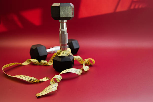 istock Black dumbbells arranged on a vibrant red background, intertwined with a measuring tape, symbolizing fitness, health, and personal training goals in a dynamic composition 2247490731