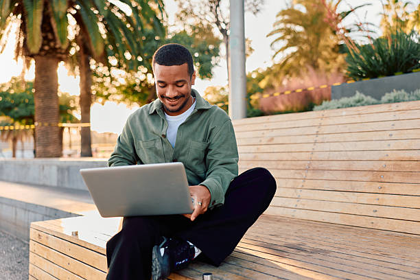 istock Young man smiling working on laptop outdoors 2247490744