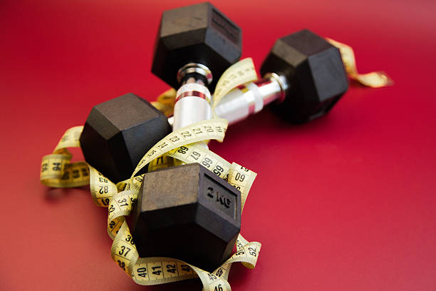 istock Black hex dumbbells wrapped with a measuring tape on a vibrant red background, symbolizing fitness, health, and the journey towards physical wellness and strength training 2247490795