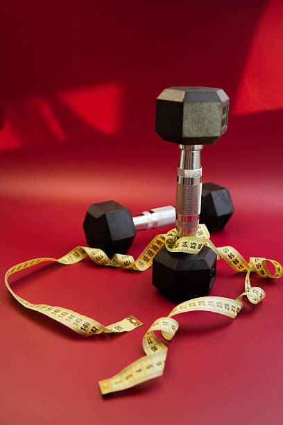 istock Black dumbbells arranged on a vibrant red background with a measuring tape intertwined, symbolizing fitness, health, and the journey towards physical well-being and strength 2247490910