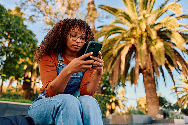 istock Young adult woman using phone outdoors in park 2247492585