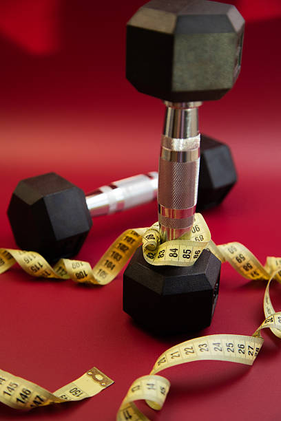 istock Black dumbbells arranged on a vibrant red background, with a measuring tape wrapped around one, symbolizing fitness, health, and personal training goals 2247493325