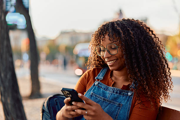 istock Young woman smiling while using phone in city 2247498847