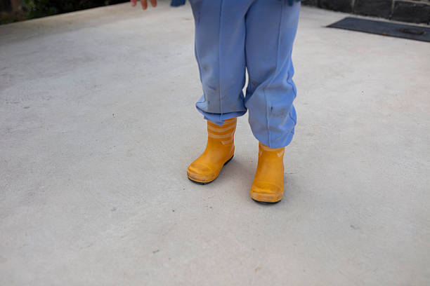 Bright yellow rubber rain boots worn by child in blue pants standing on concrete pavement
