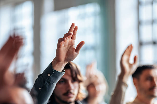 istock Business Meeting Participants Raise Hands in a Collaborative Team Setting During a Group Session Today 2247507229