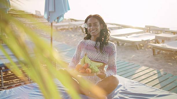 African American woman enjoying a vibrant fruit platter on the beach at sunset, with a relaxed atmosphere and tropical surroundings
