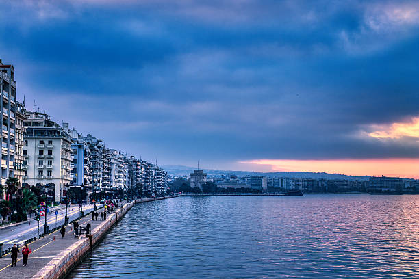 Dark clouds loom over Thessaloniki's waterfront as morning light breaks through. The White Tower stands firm, watching a city awaken beneath a shifting sky