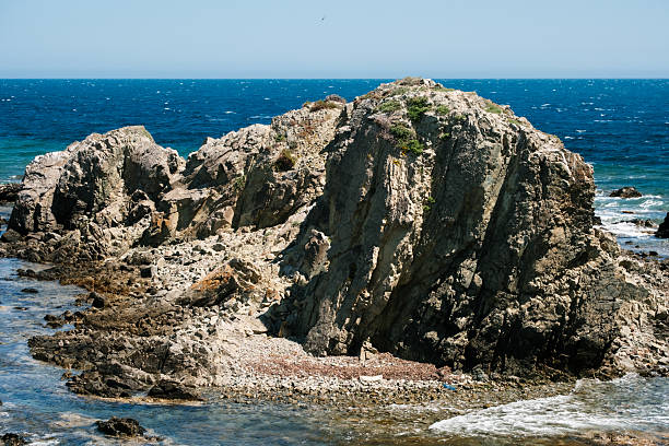 Rugged coastal rock formation against vibrant blue ocean background.