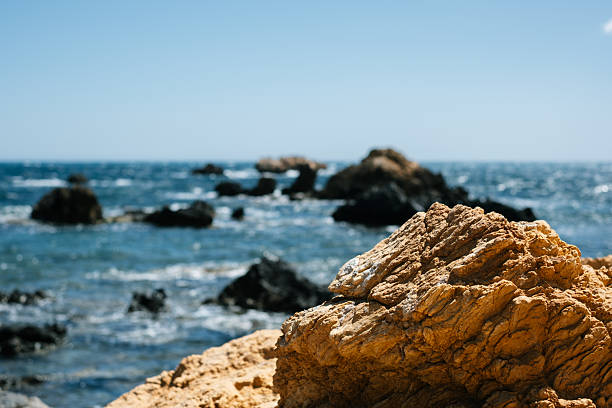Rugged coastal rocks along a clear blue ocean horizon under a sunny sky.