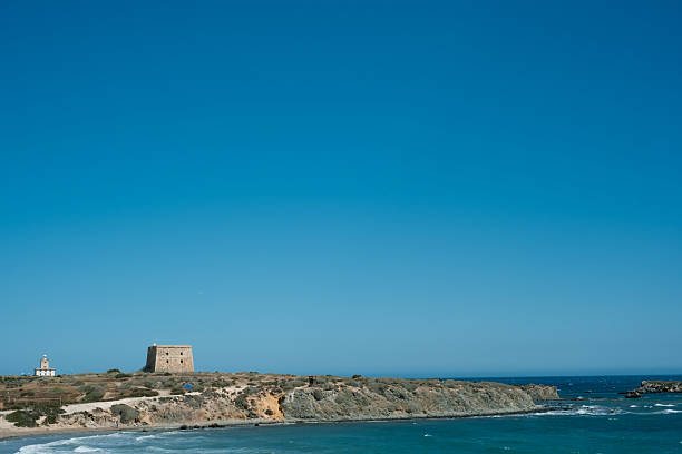 Sunny coastal landscape with historic tower and clear blue sky.