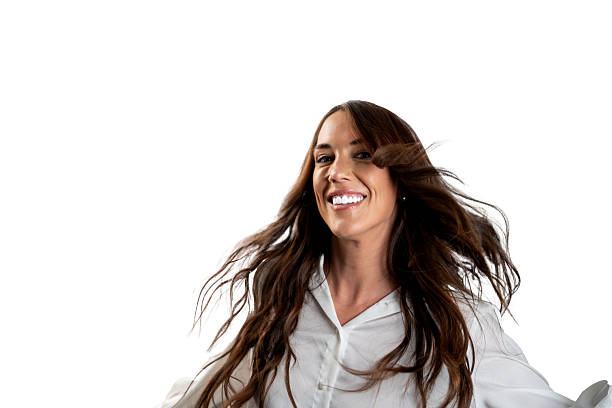 A woman with long brown hair in a white shirt experiences dynamic hair movement. Her wide smile and windswept hair suggest energy and spontaneity during the photoshoot.