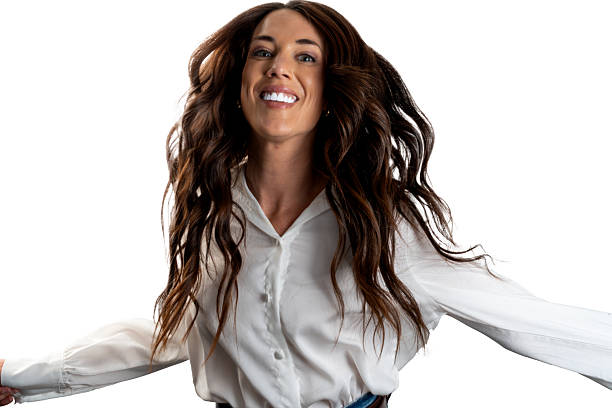 A young woman with long, flowing dark hair wearing a white button-up shirt stands with outstretched arms, expressing joy and movement against a white background. Her wide smile and dynamic pose suggest a sense of liberation and positive energy.