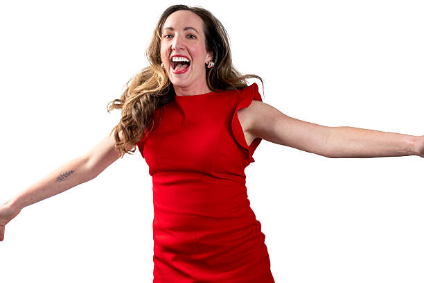 A mid-adult woman in a vibrant red dress expresses extreme happiness, with arms outstretched and head tilted back in a moment of pure excitement. Her dynamic pose and wide-open mouth convey intense emotional release against a clean white background, highlighting her uninhibited expression of joy.