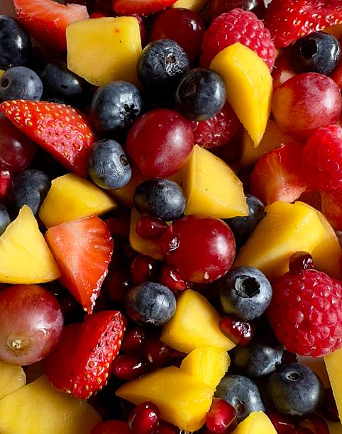 A closeup of mixed fruit including strawberries, raspberries, blueberries, grapes, pomegranate and mango. Vegetarian or vegan food.