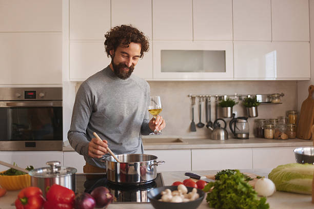 istock Man enjoying cooking dinner with wine in modern kitchen 2247524816