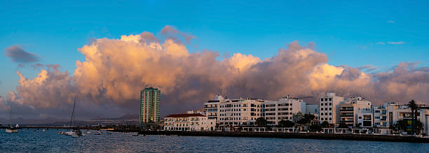 Arrecife Lanzarote waterfront view featuring historical buildings and people leisurely walking along the promenade. The serene atmosphere and clear sky create a picturesque scene on sunrise