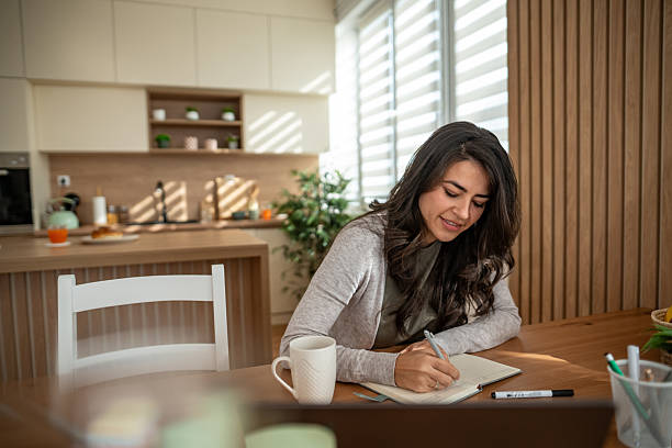 istock Young woman writing in journal at home kitchen 2247532126