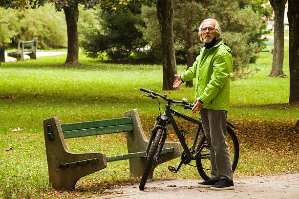 Man  in the green jacket  taking a break from cycling.  Senior man is resting in the city park.Concept of healthy lifestyle and sustainable mobility