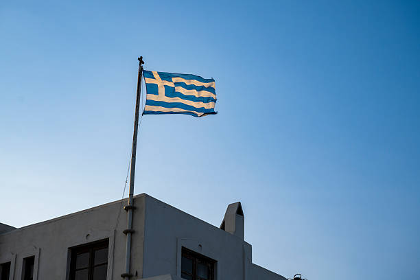 The Greek national flag flies from a rooftop pole in Naxos, Greece, standing out boldly against the clear blue sky.