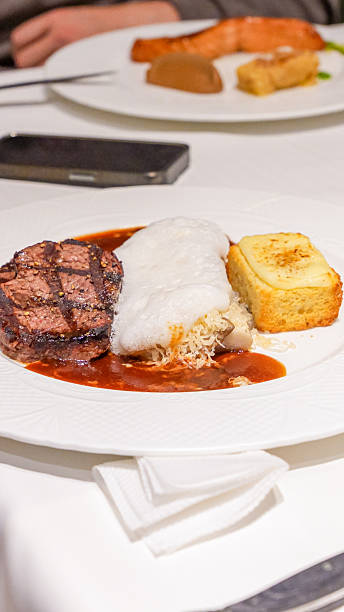 Grilled steak served with creamy sauce, fluffy mashed potatoes, and a slice of golden cornbread on a white plate, showcasing gourmet dining experience