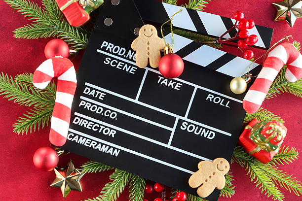 istock Image black and white film clapperboard surrounded by spruce needle twigs and red berries, felt candy canes, red and gold Christmas bauble ornaments, gingerbread men, model gift piles, stars, mottled red background, elevated view, Christmas film concept 2247536941