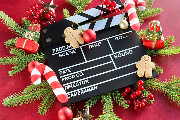 istock Image black and white film clapperboard surrounded by spruce needle twigs and red berries, felt candy canes, red and gold Christmas bauble ornaments, gingerbread men, model gift piles, stars, mottled red background, elevated view, Christmas film concept 2247536975