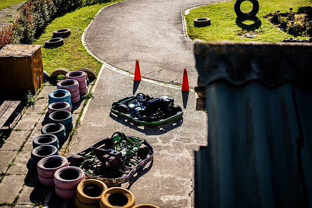 A professional go-kart racing circuit featuring multiple racing karts parked on a curved concrete track. The track is bordered by grassy areas and lined with colorful tires used as safety barriers, with safety cones marking specific zones of the course.